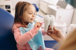 A Small Girl In Dental Clinic Brushing Big Artificial Teeth