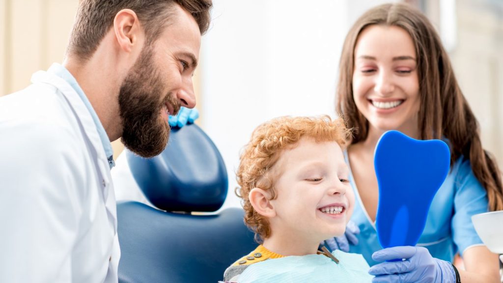 Child Smiling At The Dentist With A Dental Assistant